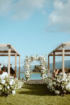 an outdoor ceremony with white flowers and greenery on the aisle, along with people sitting in chairs