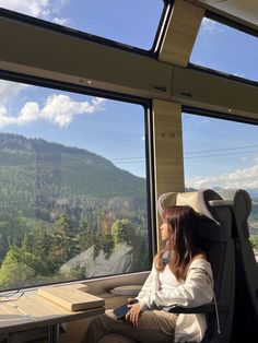 a woman sitting in a train car looking out the window at mountains and trees outside