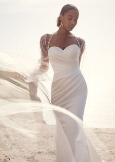 a woman standing on top of a sandy beach next to the ocean wearing a wedding dress