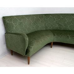 a green couch sitting on top of a hard wood floor next to a white wall