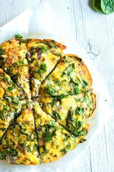 an omelet with spinach and cheese is on a white plate next to some green leaves