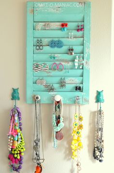 an old shutter is used as a jewelry holder for necklaces and bracelets hanging on the wall