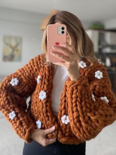 a woman taking a selfie in front of her phone wearing an orange knitted cardigan