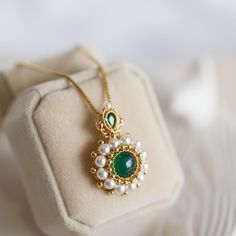 Inspired by the beauty of nature, this one-of-a-kind pendant necklace offers a stunning blend of green Chalcedony, crystal Pearl, and faceted green Cubic set in a 14K gold filled and hung on a box chain. Experiencing the beauty of this piece requires more than words or images; the unique design and the rich green colour stone is truly beautiful. Whether worn alone for a subtle statement or layered with other necklaces for a more sophisticated look, the Skylar Green Chalcedony Necklace adds an ef Round Green Emerald Necklace With Jewels, Elegant Emerald Necklace With Large Pendant, Elegant Green Long Necklace, Elegant Long Green Necklaces, Elegant Long Green Necklace, Jade Pendant Necklaces For Crafting, Exquisite Round May Birthstone Necklace, Green Crystal Pendant Jewelry, Green Round Pendant Clavicle Chain