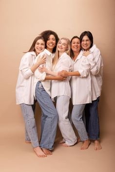 four women in white shirts and jeans are posing for a photo with their arms around each other