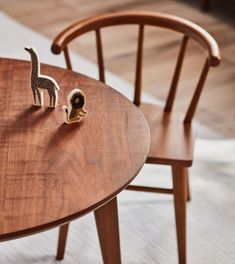 two toy giraffes sitting on top of a wooden table next to a chair