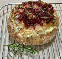 a baked bread with cranberry sauce and herbs on top sits on a cooling rack