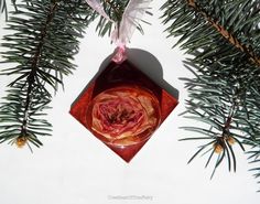 an ornament hanging from a pine tree with a red rose in the center