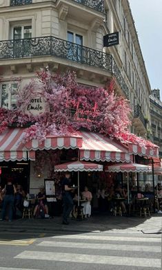 people sitting at tables under umbrellas in front of a building with red and white awnings