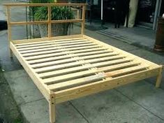 a wooden bed frame sitting on the side of a sidewalk next to a planter