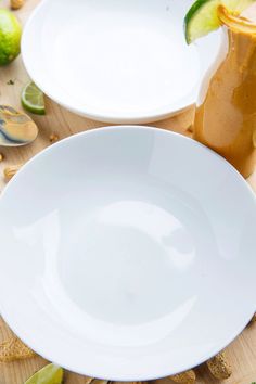 two white plates sitting on top of a wooden table next to limes and peanuts