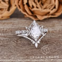 a white diamond ring sitting on top of a wooden table next to a rose flower