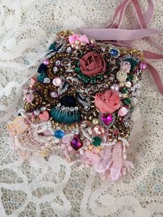 a small purse with lots of beads and flowers on it sitting on a lace covered surface