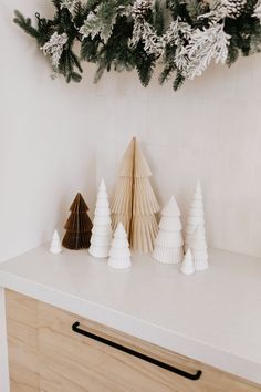 three paper christmas trees sitting on top of a white counter next to a wooden cabinet