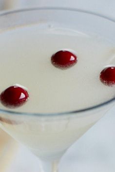 two cherries are placed on the rim of a martini glass filled with white liquid