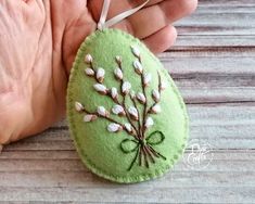 a hand is holding a green felt ornament with white flowers and leaves on it