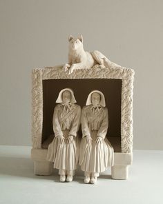 two figurines sitting on top of a white box with a dog in the background