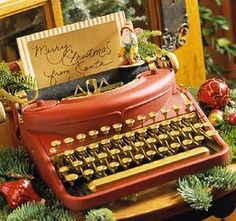 an old fashioned red typewriter sitting on top of a wooden table next to christmas decorations