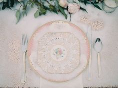 an empty plate and silverware on a table with floral arrangements in the back ground