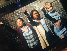 two women are standing in front of a brick wall and one is pointing at the camera