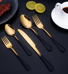 four forks, two spoons and one knife on a black table with lemon slices