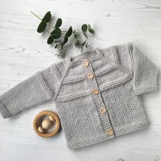 a knitted cardigan and wooden toy on a white wood table with eucalyptus leaves