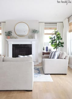 a living room with two couches and a fireplace in the corner, surrounded by potted plants