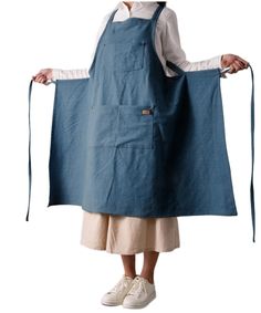 a woman wearing an apron and white shirt holding up a blue piece of cloth in her hands