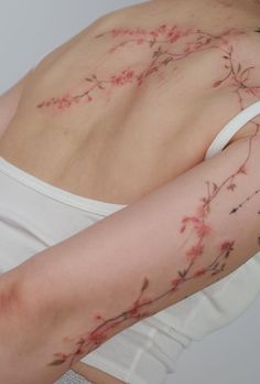 a woman's back with tattoos on her left arm and the top half of her body covered in pink flowers