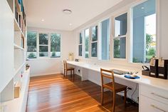 an empty room with wooden floors and white walls, has two desks in front of large windows