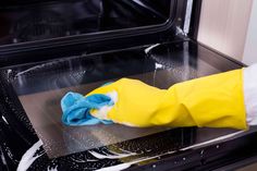 a person in yellow gloves cleaning an oven with a blue and white rag on it