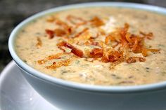 a white bowl filled with soup and bacon on top of a saucer next to a spoon