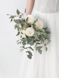 a bride holding a bouquet of white roses and greenery