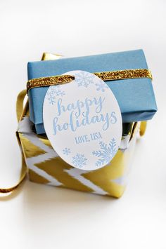 a gift wrapped in blue and gold with a tag that says happy holidays