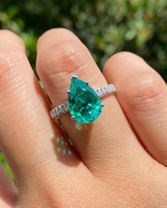 a close up of a person's hand holding a ring with a green stone