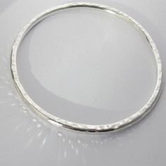 A solid silver hammered bangle, the texture adds extra interest as it catches the light.  A contemporary, timeless piece of jewellery which looks striking worn on it's own or with other bangles and bracelets. This is a solid sterling silver bangle, it is 3mm thick and 21cm in circumference and 6.8cm in diameter. The bangle is hallmarked with my unique makers mark by the London Assay Office and comes packaged in a gift box. This is part of my hammered collection of Scandinavian style jewellery wh Hammered Sterling Silver Bangle Bracelet, Silver Hammered Round Bangle, Hammered Silver Round Bangle, Minimalist Silver Hammered Bangle, Minimalist Hammered Silver Bangle, Modern Hammered Round Bracelets, Minimalist Hammered Sterling Silver Bangle, Minimalist Hammered Sterling Silver Bangle Bracelet, Minimalist Hammered Round Bangle