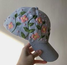 a hand is holding up a hat with flowers on the front and side of it