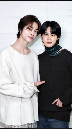 two young men standing next to each other in front of a white wall and wearing sweaters