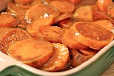 cooked carrots are in a green and white casserole dish with sauce on top