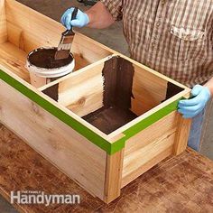 a man in blue gloves is painting the inside of a wooden box with green trim