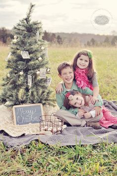 two children sitting on a blanket in front of a christmas tree with a chalkboard sign