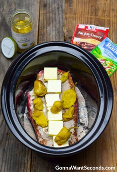 a crock pot filled with food sitting on top of a wooden table next to some butter