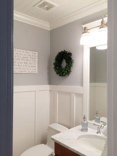 a white toilet sitting next to a bathroom sink under a green wreath on the wall