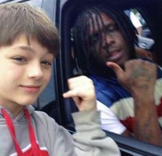 a young man with dreadlocks sitting in a car next to another person holding his hand up