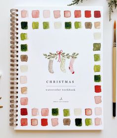 the christmas watercolor workbook is next to two pencils and an ornament