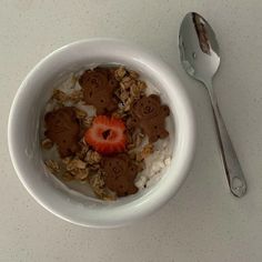 a bowl filled with granola and topped with strawberries next to a silver spoon