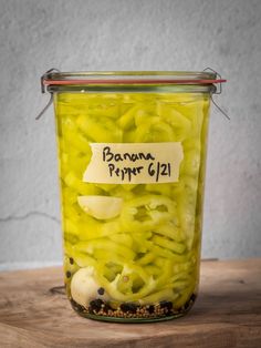 a jar filled with pickled green peppers on top of a wooden table