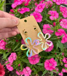 a person holding up a pair of earrings in front of pink flowers