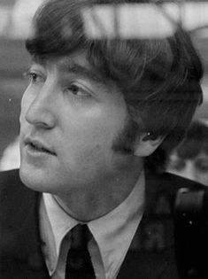 black and white photograph of man in suit looking out the window at another person standing behind him