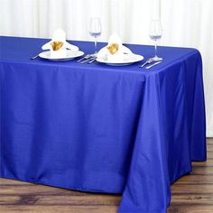 a blue table cloth with two white plates and silverware on it next to wine glasses